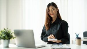 Confident woman sitting at desk with laptop and phone, symbolizing financial planning and researching the best HSA options for 2025.