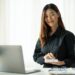Confident woman sitting at desk with laptop and phone, symbolizing financial planning and researching the best HSA options for 2025.