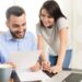 Smiling couple reviewing documents at home, representing individuals researching Colorado Medicaid income limits and eligibility requirements.