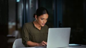 Woman focused on laptop screen at night, researching Colorado open enrollment options after missing the deadline.
