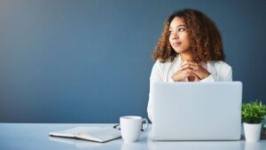 Thoughtful woman sitting at desk with laptop, symbolizing planning and decision-making about Colorado Medicaid inheritance and asset protection.