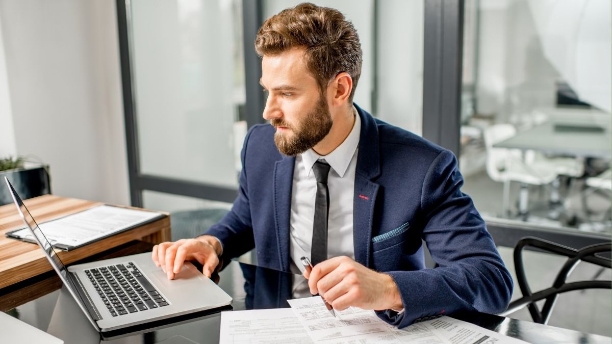 Professional man reviewing documents and working on laptop, representing analysis of the advanced premium tax credit and health insurance costs.