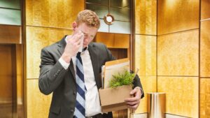 Upset man leaving his job with a box of personal belongings, representing the question how long do you have health insurance after leaving a job.