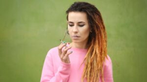 Woman with dreadlocks in a pink sweatshirt holding a joint, representing the question is weed covered by insurance.